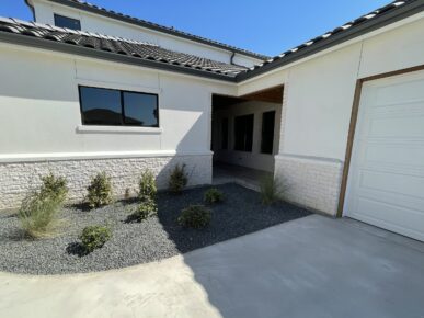 A house with a garage and plants in the front yard.