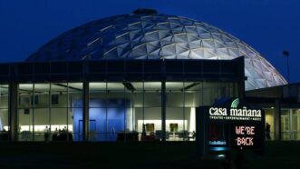 A large dome lit up at night in front of a building.
