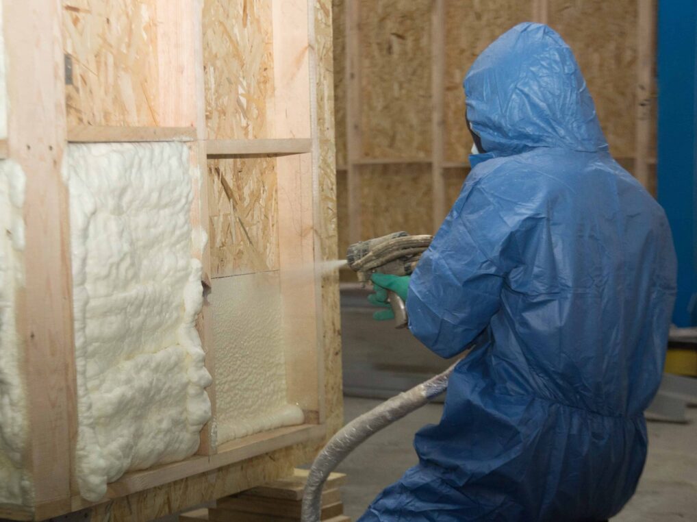 A man in a blue suit is spraying insulation in a room.