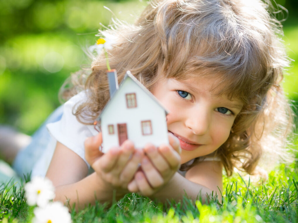 A little girl laying on the grass with a model house.